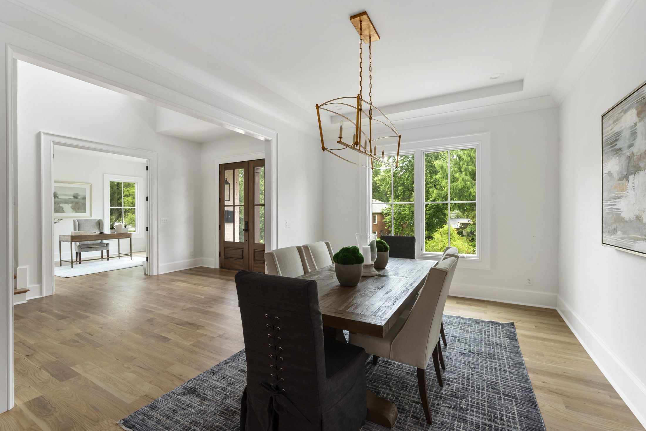 Formal dining room with tray ceiling, brass linear chandelier, and reclaimed-wood table open to the foyer — Bywood by Stillman Properties Charlotte NC