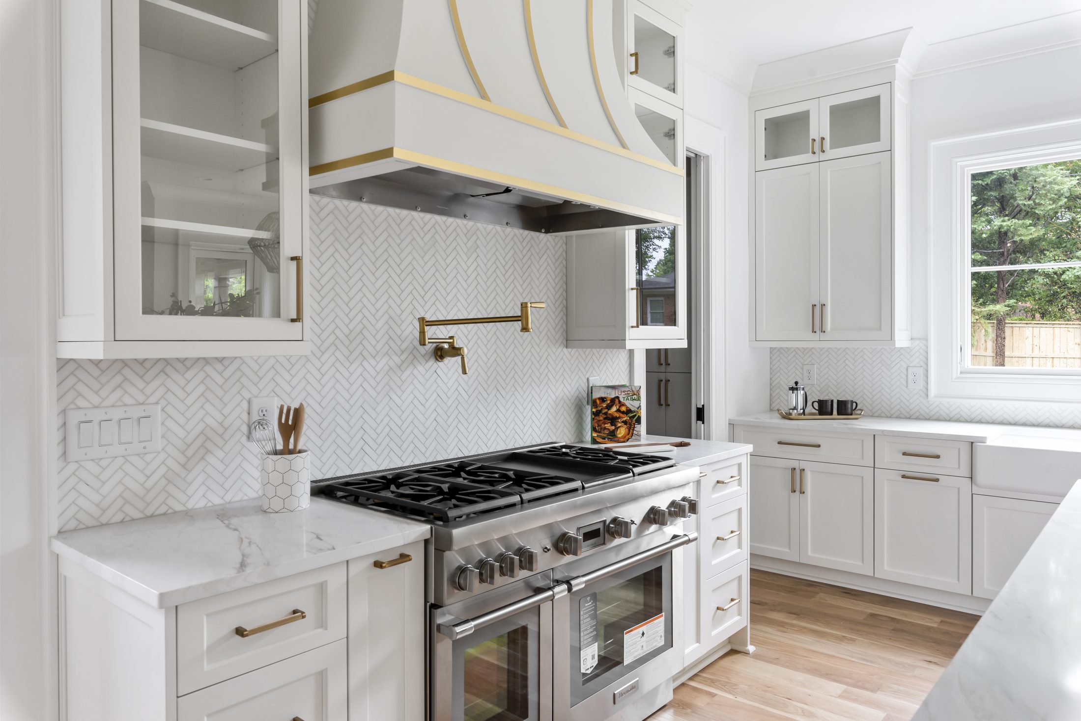Kitchen range wall with pro-grade stainless range, custom hood, and herringbone tile backsplash — Bywood by Stillman Properties Charlotte NC