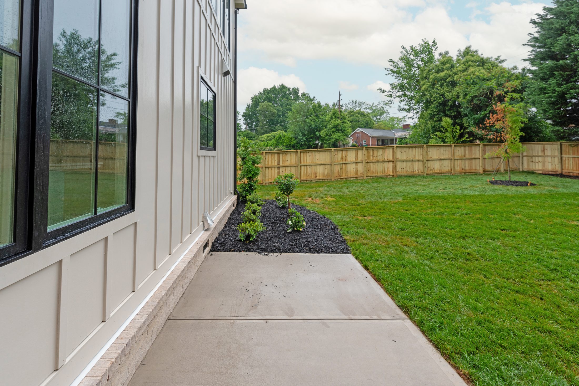 Side yard with new landscaping, mulched beds, and concrete walkway alongside the board-and-batten exterior — Bywood by Stillman Properties Charlotte NC