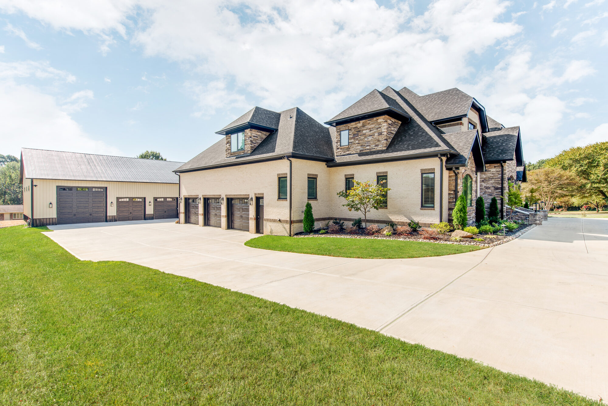 Side elevation of Coddle Creek showing the home's three-car garage and the barndominium beyond — Stillman Properties Concord NC
