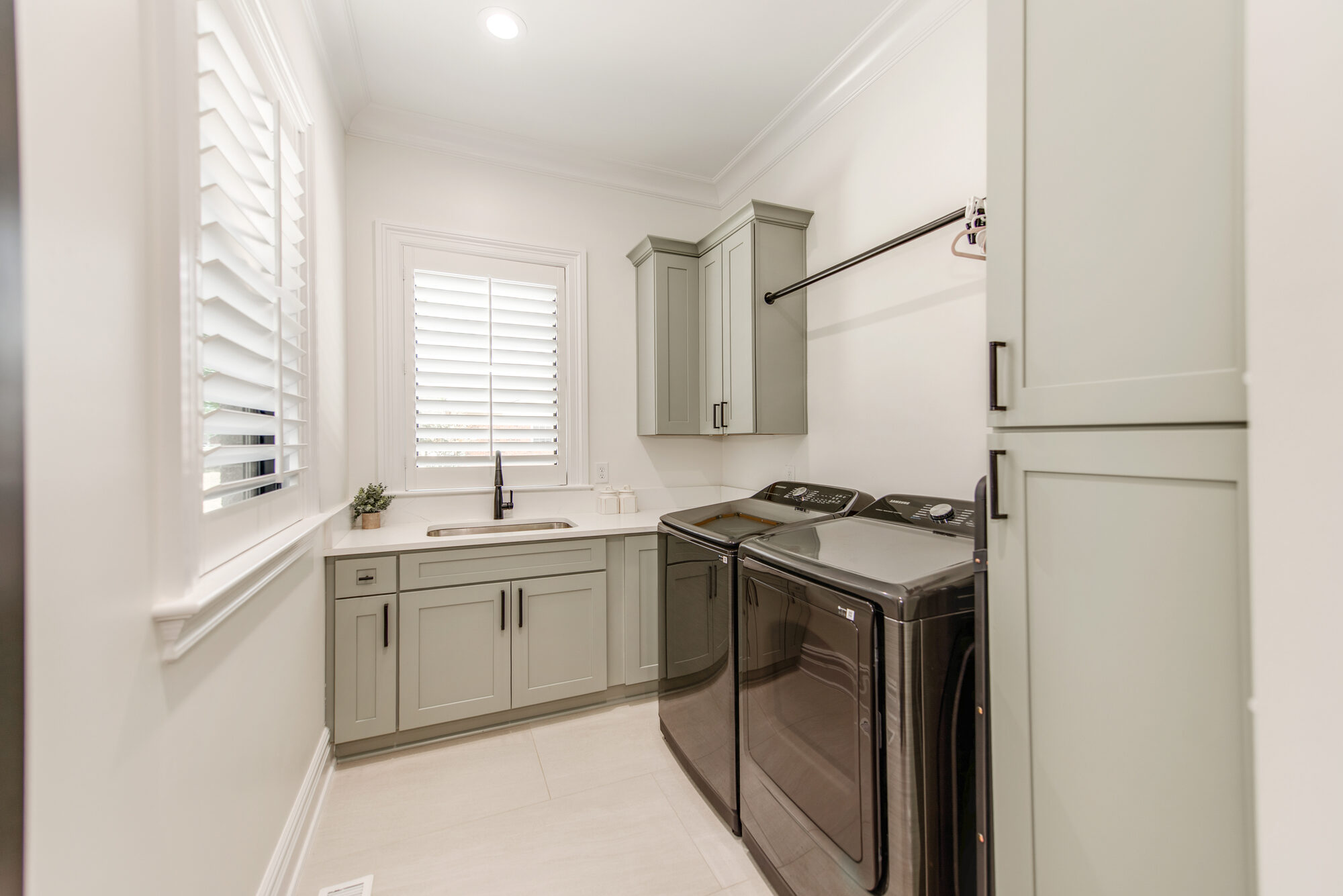 Laundry room with sage cabinetry, plantation shutters, and built-in hanging rod — Coddle Creek by Stillman Properties Concord NC