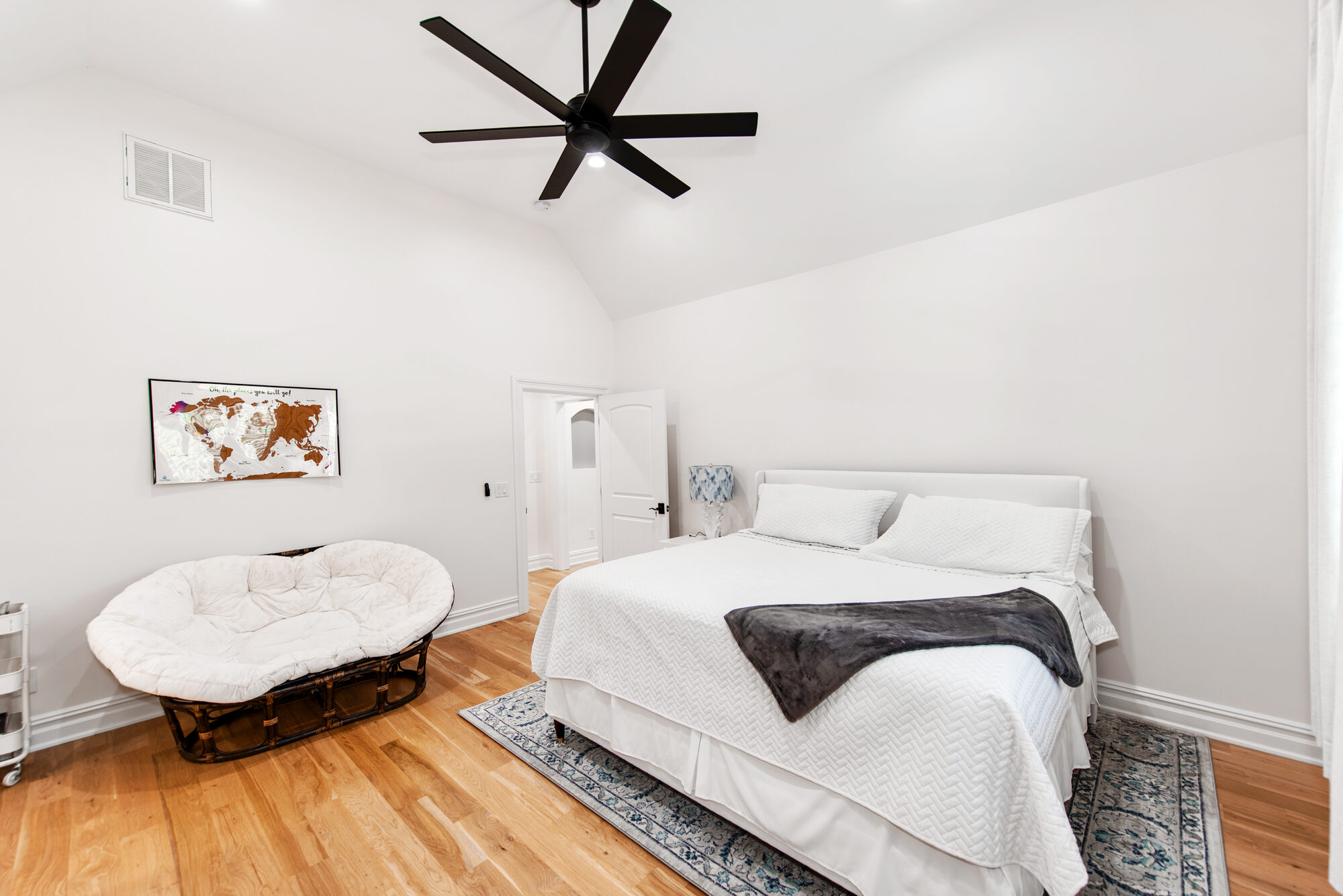 Guest suite with rattan papasan reading chair and travel-map artwork — Coddle Creek by Stillman Properties Concord NC