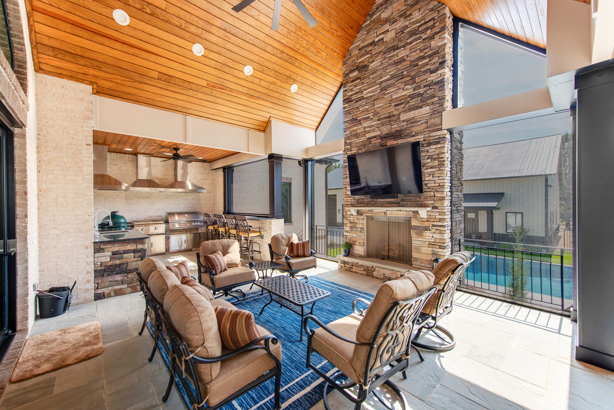 Covered patio with vaulted cedar ceiling, floor-to-ceiling stacked stone fireplace, mounted television, and full outdoor kitchen — Coddle Creek by Stillman Properties Concord NC