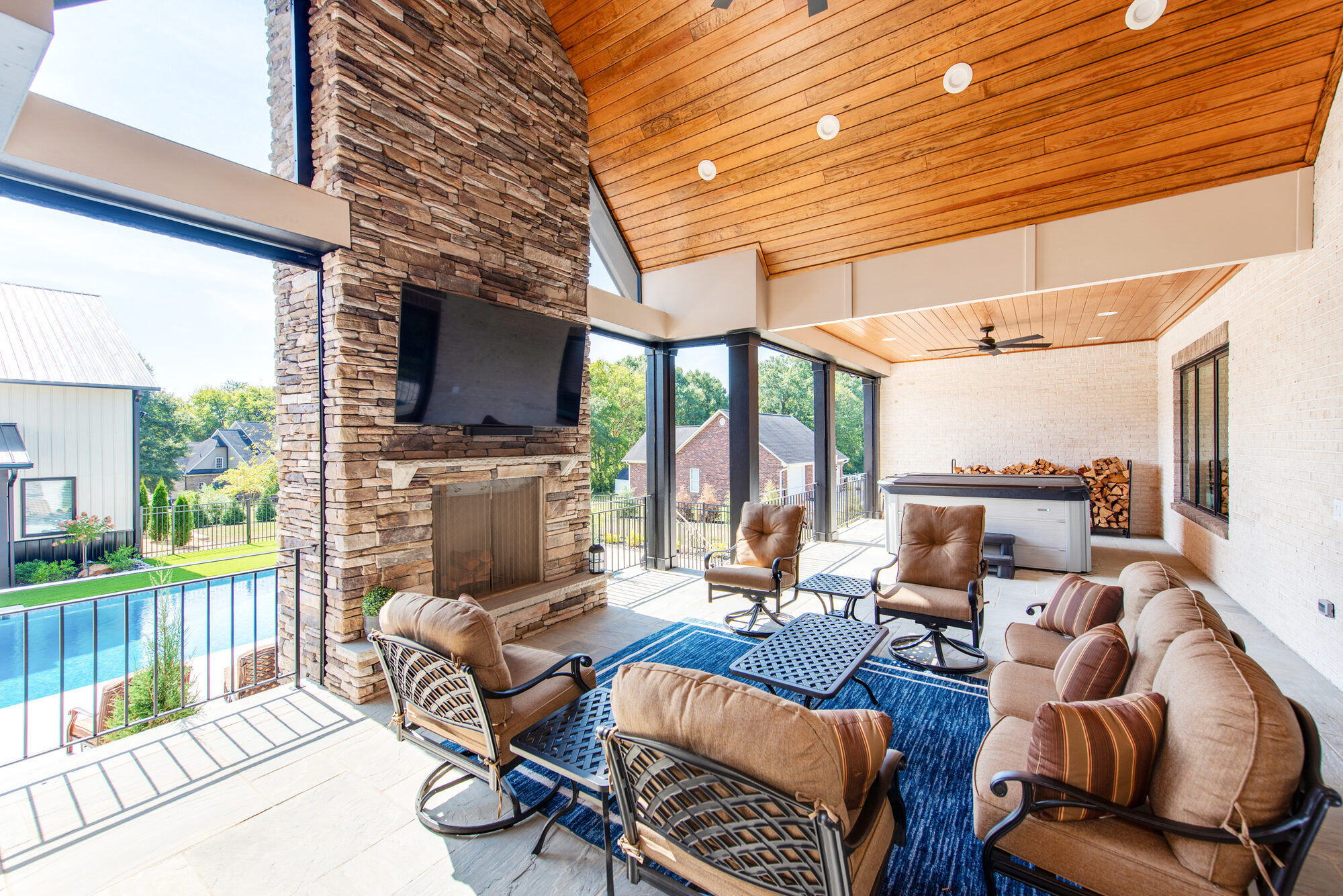 Covered patio reverse angle showing the stone fireplace, hot tub, and view to the pool — Coddle Creek by Stillman Properties Concord NC