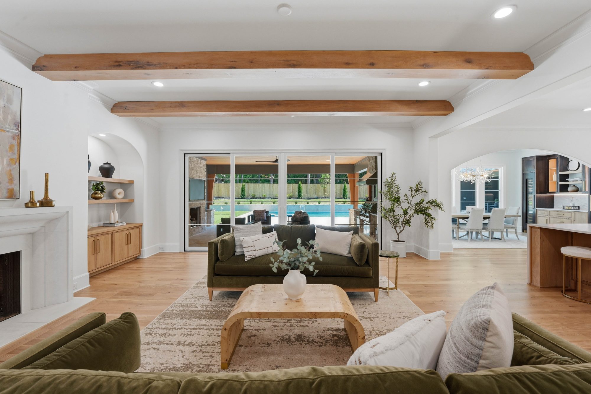 Living room view toward kitchen with wood beams and arched alcove built-ins — Creola custom home in Charlotte NC by Stillman Properties