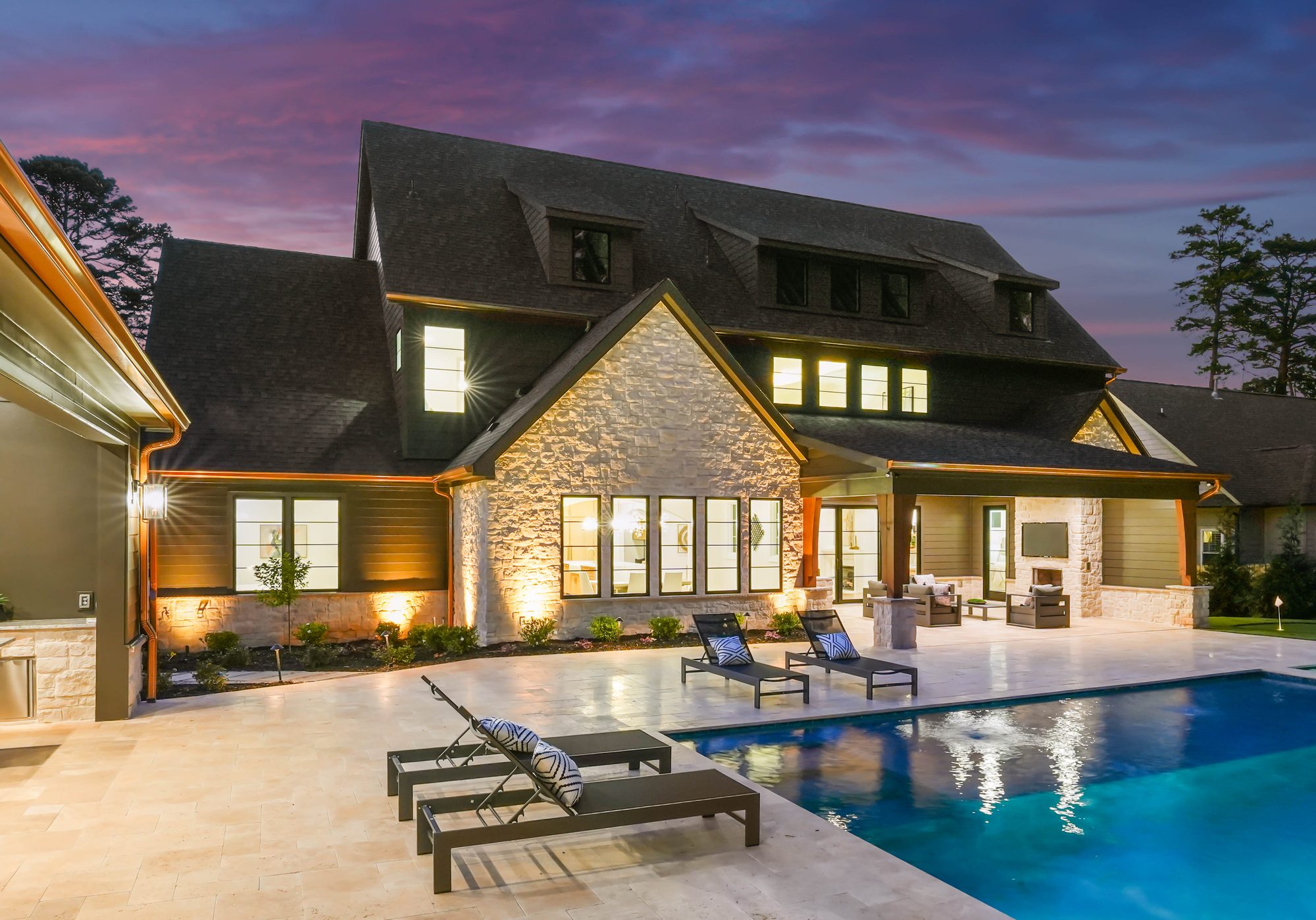 Resort-style pool and travertine deck at twilight with warm house glow — Creola custom home in Charlotte NC by Stillman Properties