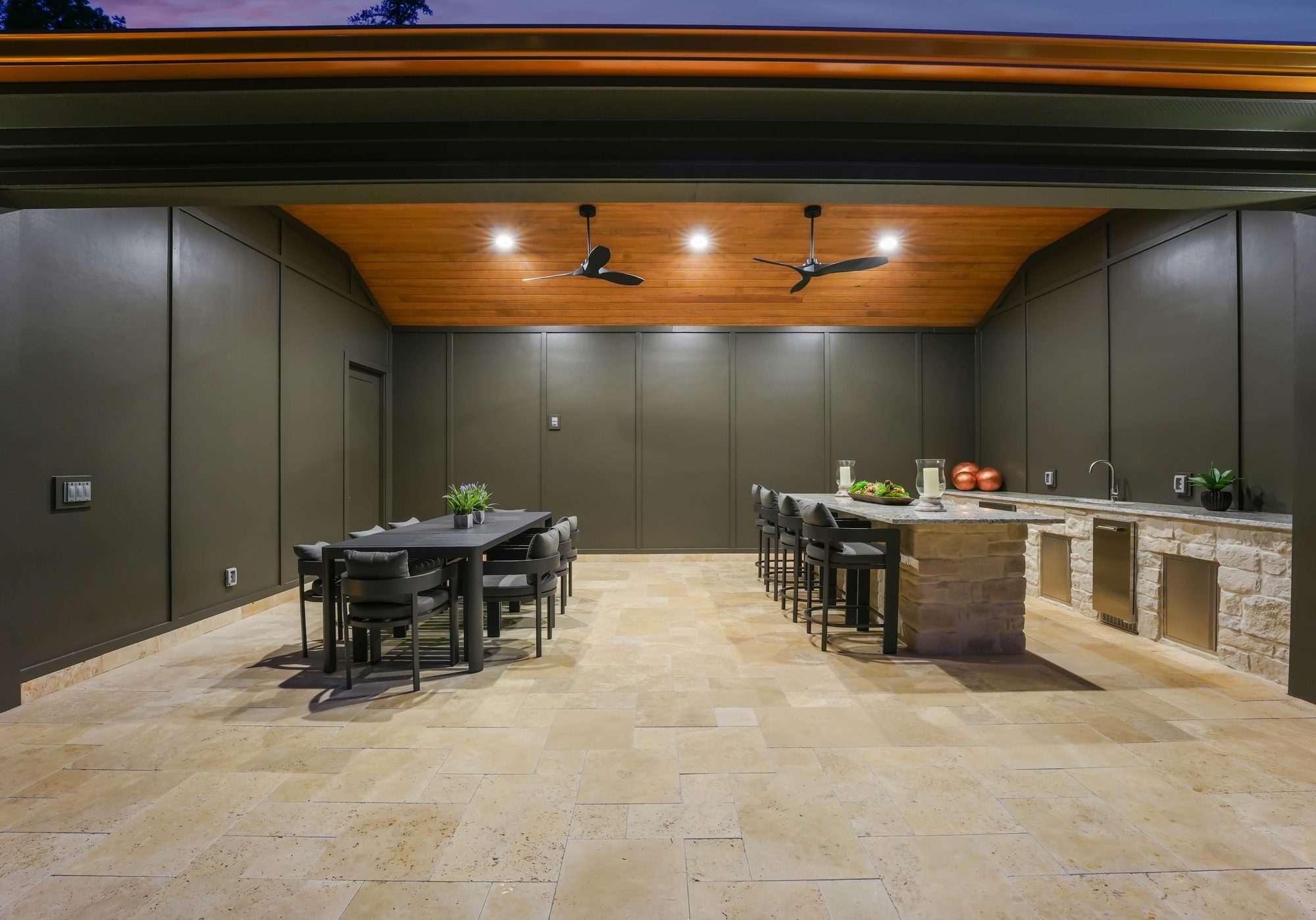 Pool cabana interior at twilight with island, dining table, and wood ceiling — Creola custom home in Charlotte NC by Stillman Properties