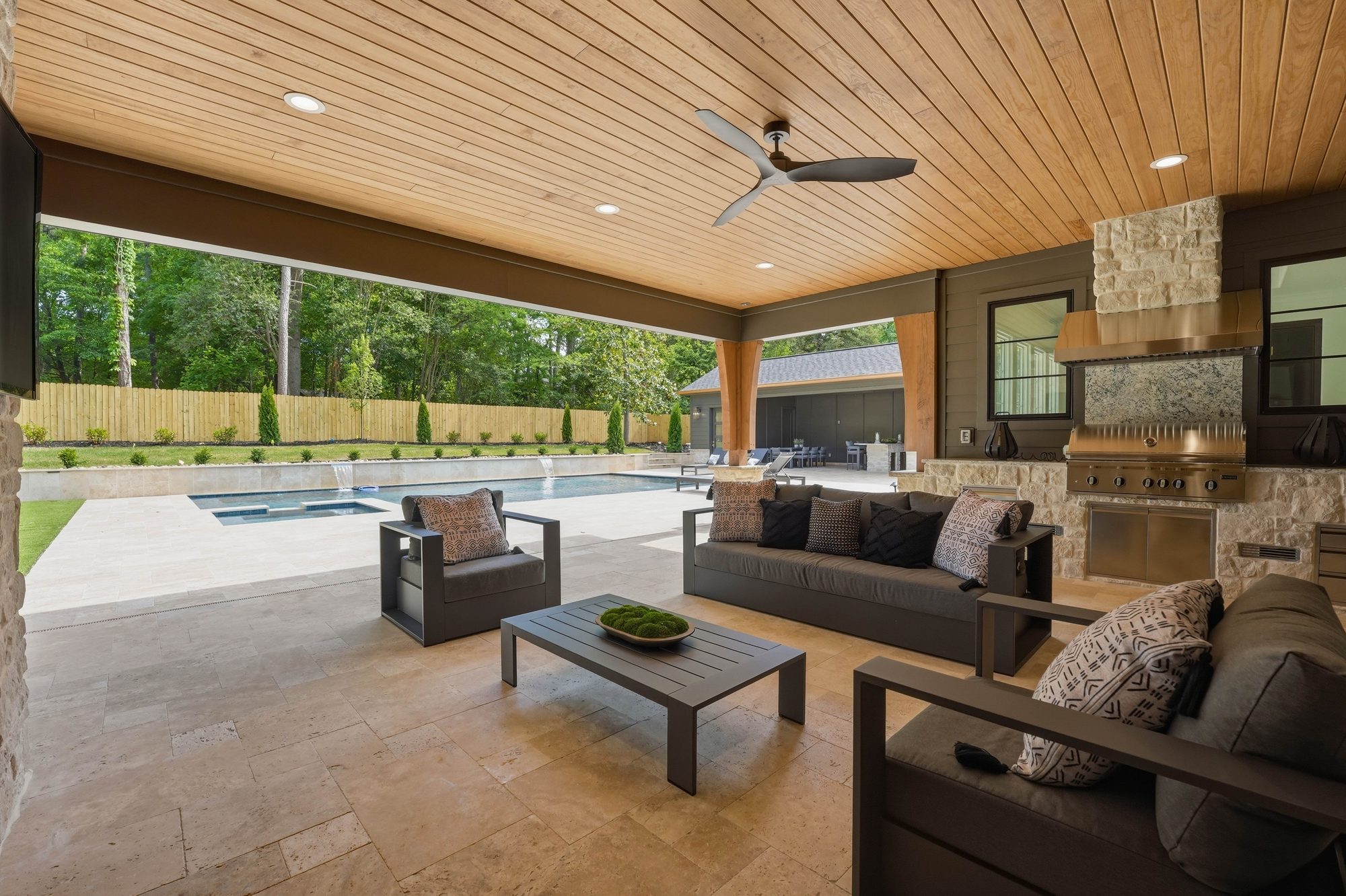 Covered outdoor living room with sliding walls fully open to the pool and travertine deck — Creola custom home in Charlotte NC by Stillman Properties