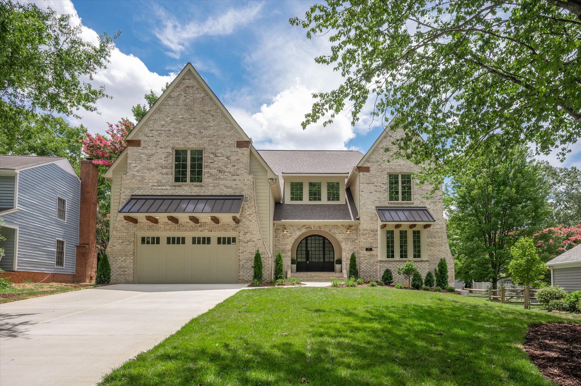 Front elevation of Heather in daylight showing buff brick, painted lap siding, twin steep gables, and a two-car garage with standing-seam awning — Heather by Stillman Properties Charlotte NC