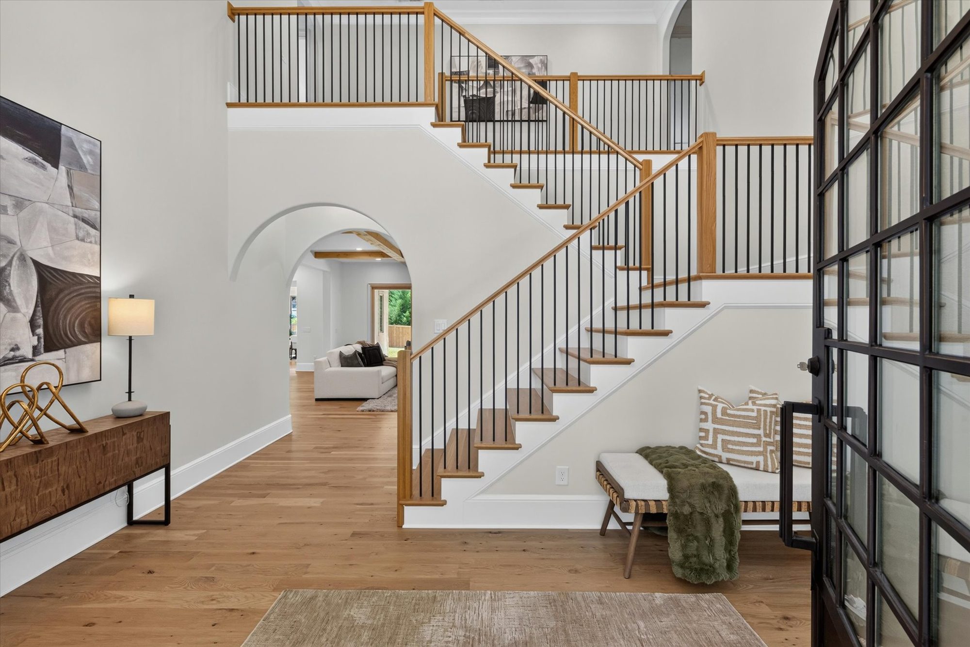 Two-story foyer at Heather with white oak stair treads, slim iron balusters, open upper landing, and a barrel-arched passage to the great room — Heather by Stillman Properties Charlotte NC