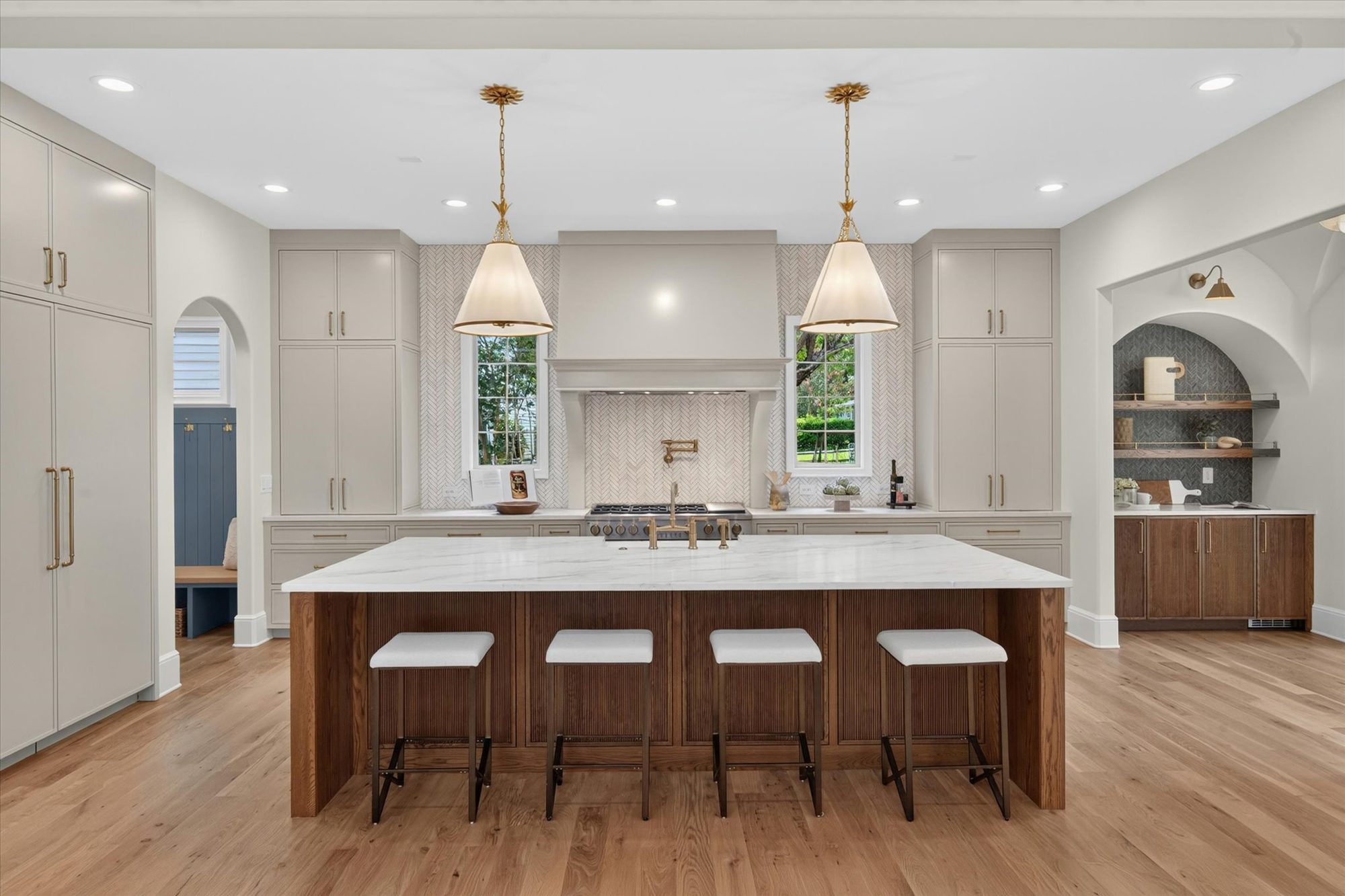 Kitchen at Heather with oversized fluted white oak island in marble, brass cone pendants, custom plaster hood, and herringbone backsplash — Heather by Stillman Properties Charlotte NC