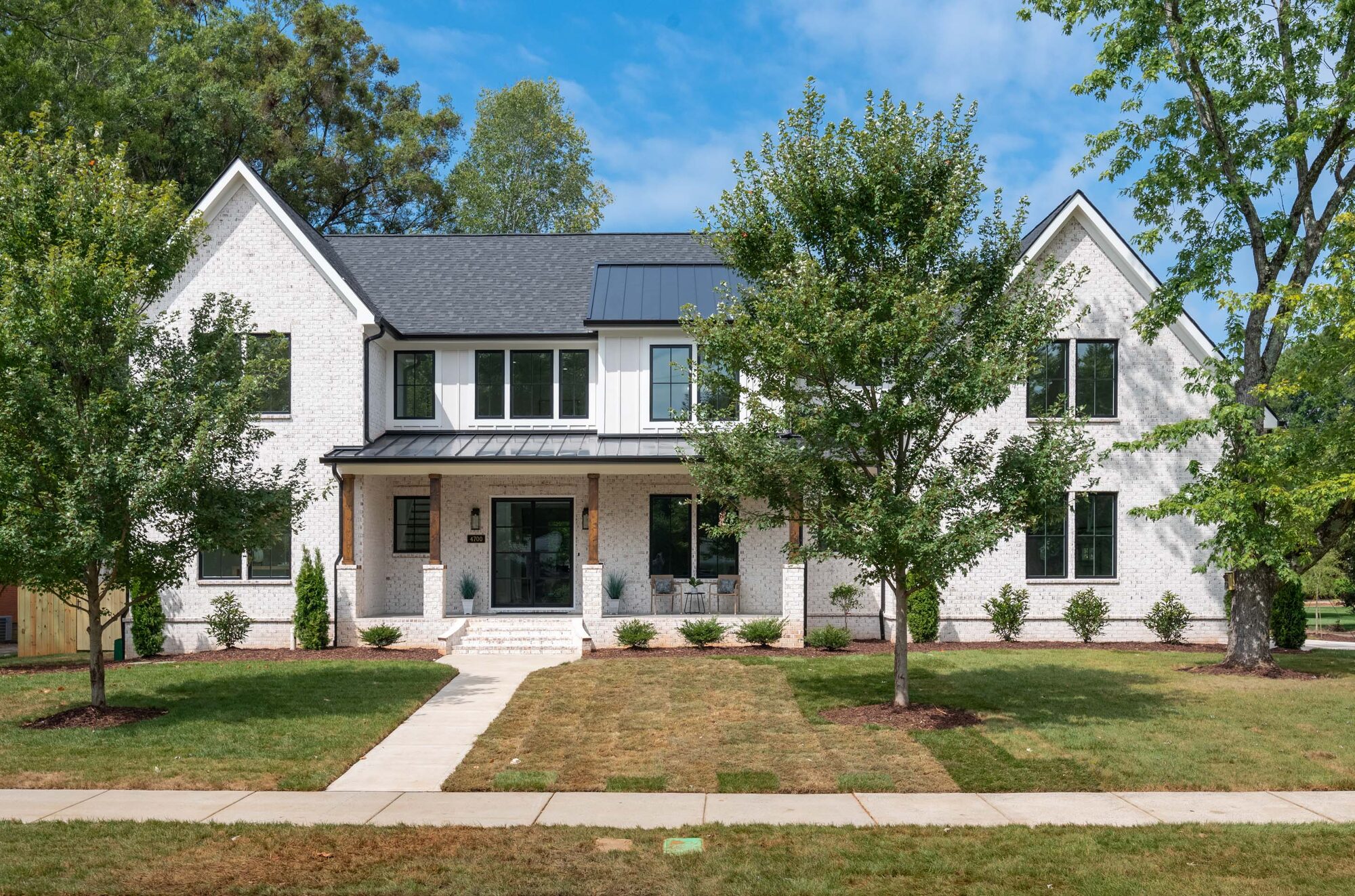 Walker front exterior with twin gables, whitewashed brick, and standing seam metal porch roof — transitional custom home by Stillman Properties Cotswold Charlotte NC