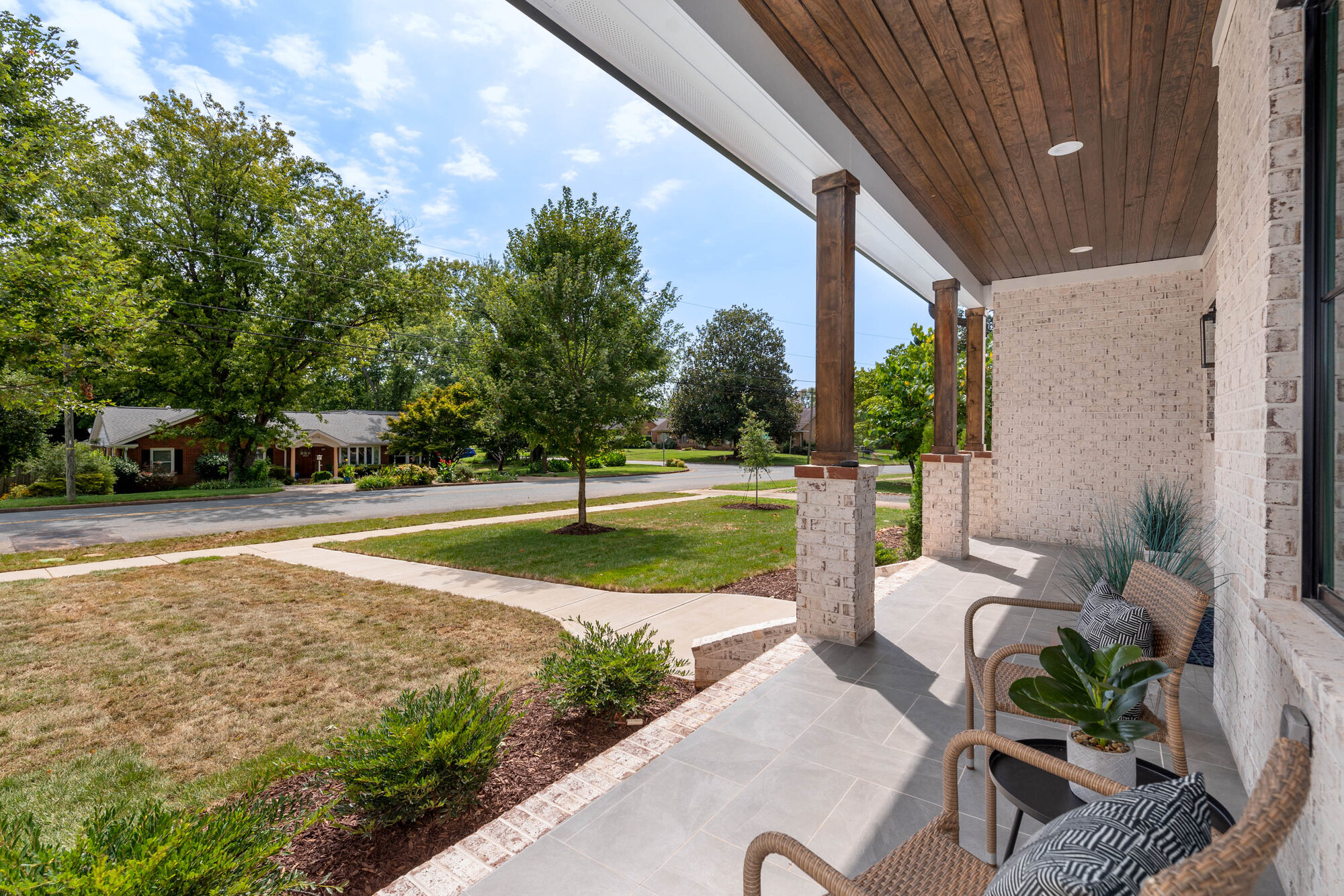 Walker front porch with cedar columns, stained tongue-and-groove ceiling, slate tile floor, and woven wicker seating — Stillman Properties Cotswold Charlotte NC