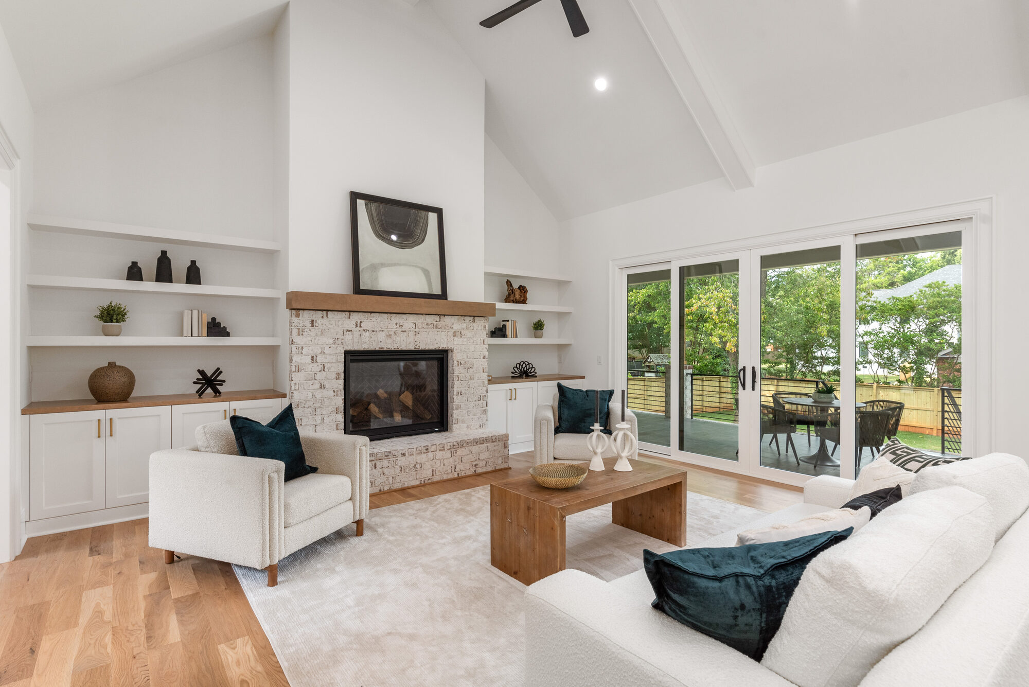 Walker great room fireplace wall with floating walnut mantel, whitewashed brick surround, and flanking white floating shelves — Stillman Properties Cotswold Charlotte NC